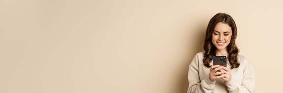 Frau mit Handy vor beigem Hintergrund