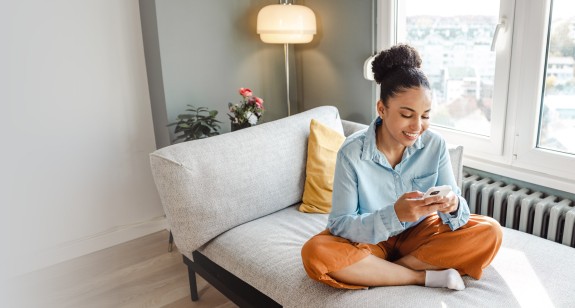 Frau sitzt auf einem Sofa in Grau mit Handy in der Hand