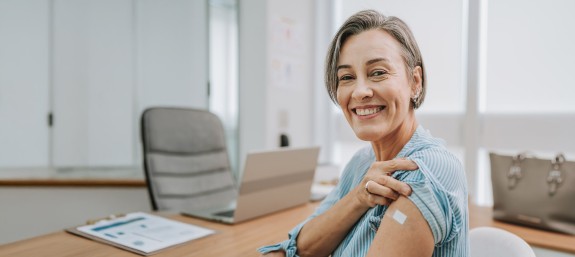 Frau zeigt Impfpflaster auf ihrem Oberarm